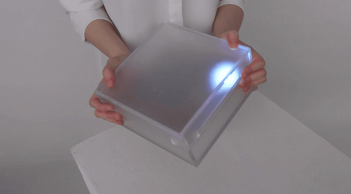 A hand-held frosted box with a glowing point of light inside, tilted so the light falls toward one corner.